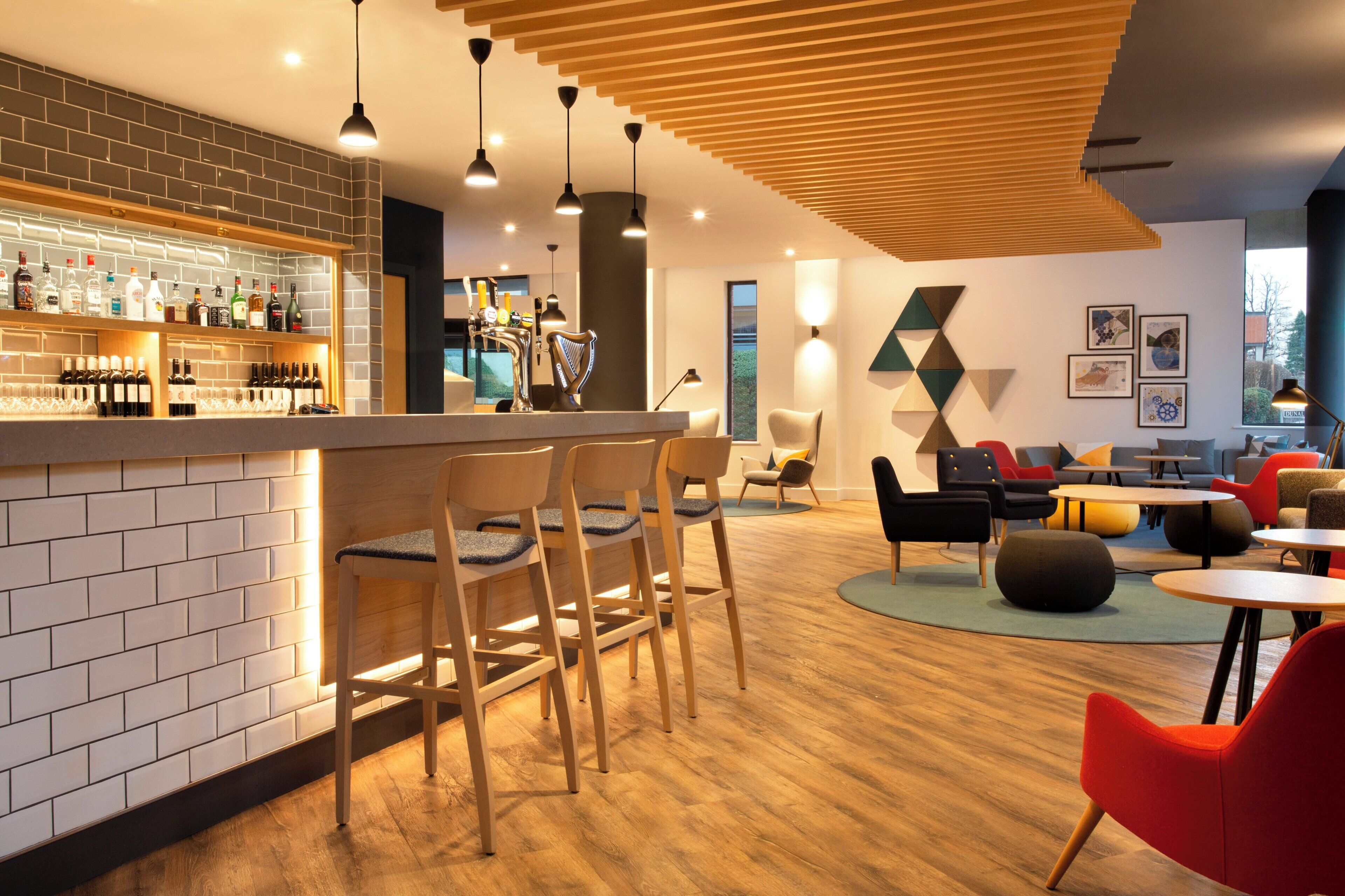 A modern bar area with a brick wall, wooden chairs, and a variety of bottles.