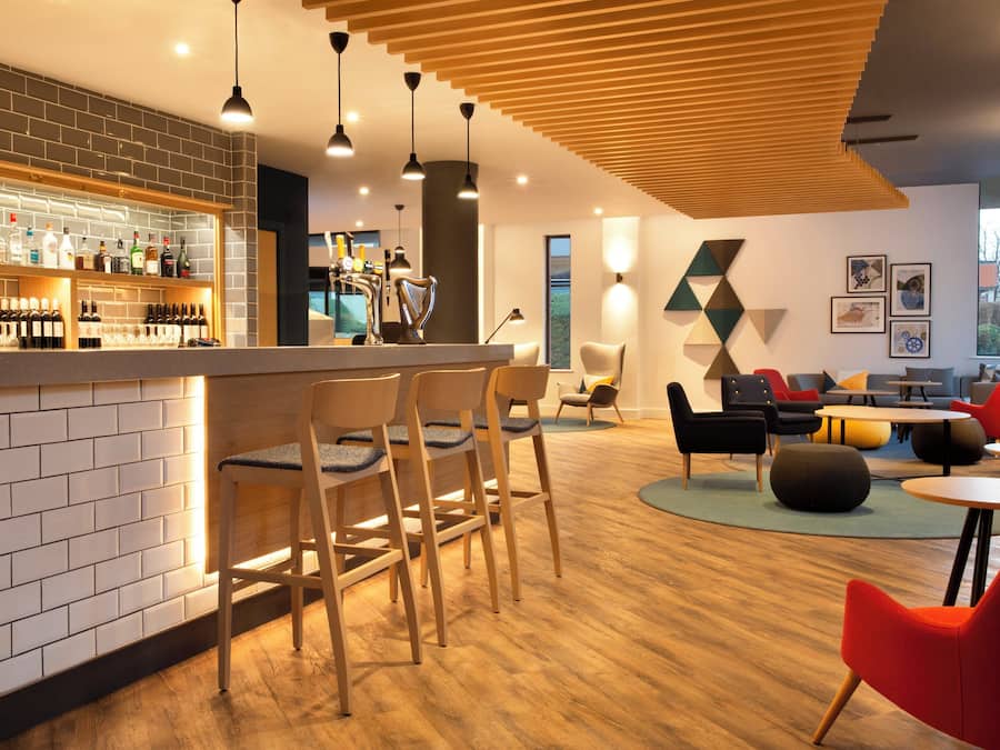 A modern bar area with a brick wall, wooden chairs, and a variety of bottles.