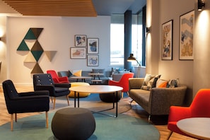 Un espace lounge moderne, doté de différents types de sièges, d’œuvres d’art accrochées aux murs et offrant une vue sur la rue.