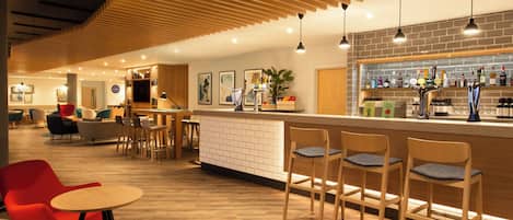 A modern bar area with wooden flooring, bar stools, and a variety of liquor bottles.