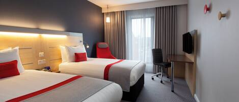 A hotel room with two beds, a desk, a chair, a television, and a window with curtains.