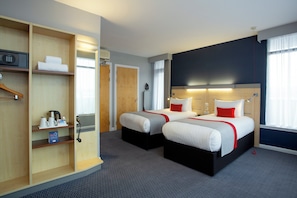 A hotel room with two beds, a minibar, a desk, and a wardrobe.