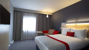 Habitación de hotel con una cama grande, una mesita pequeña, un sofá y un televisor en la pared.