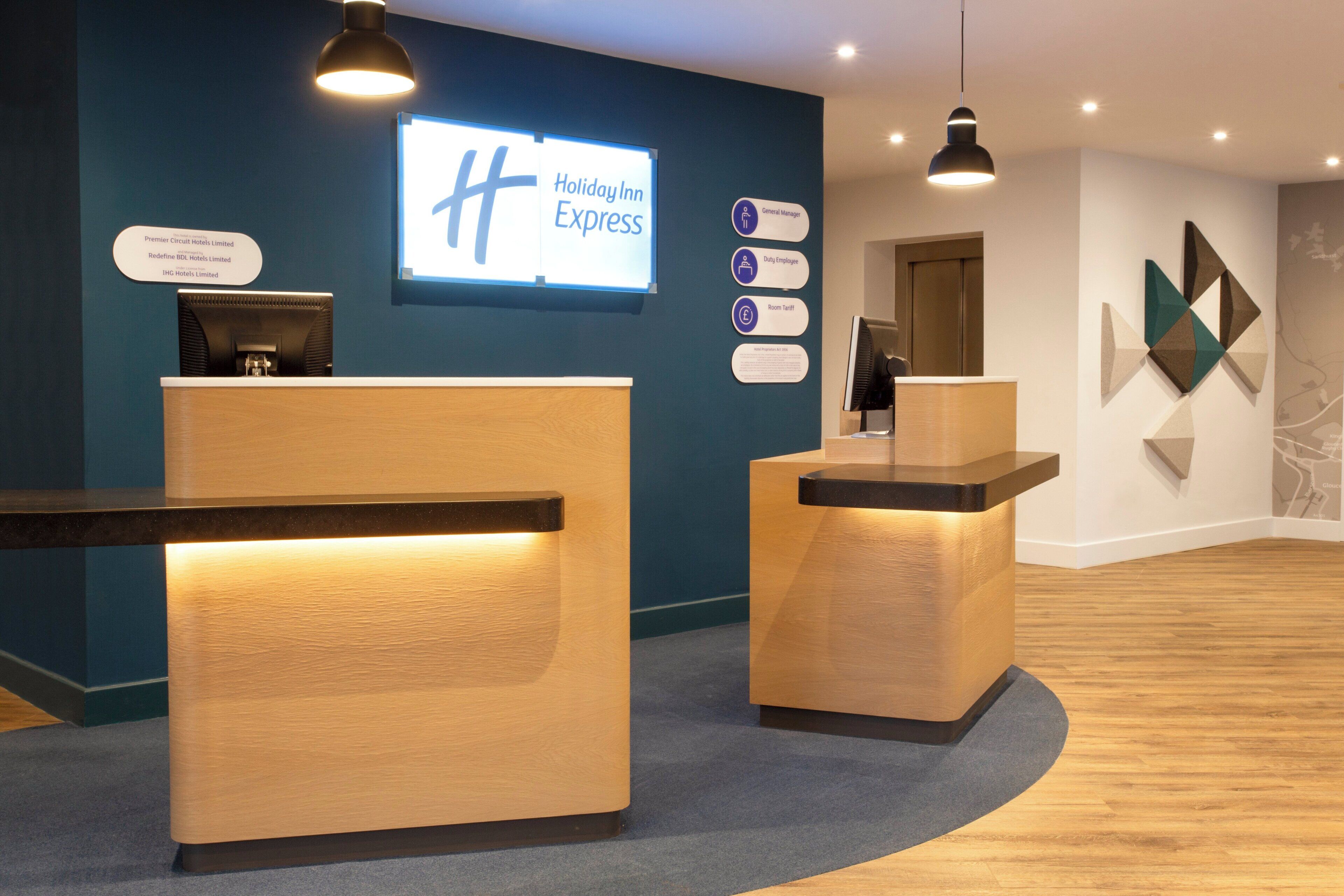 A reception desk area with a digital display, a sign indicating 'Holiday Inn Express', and a wall-mounted information board with various hotel details.