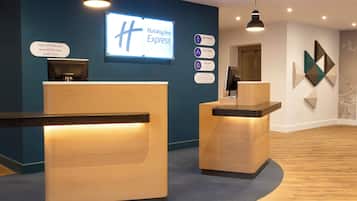 A reception desk area with a digital display, a sign indicating 'Holiday Inn Express', and a wall-mounted information board with various hotel details.