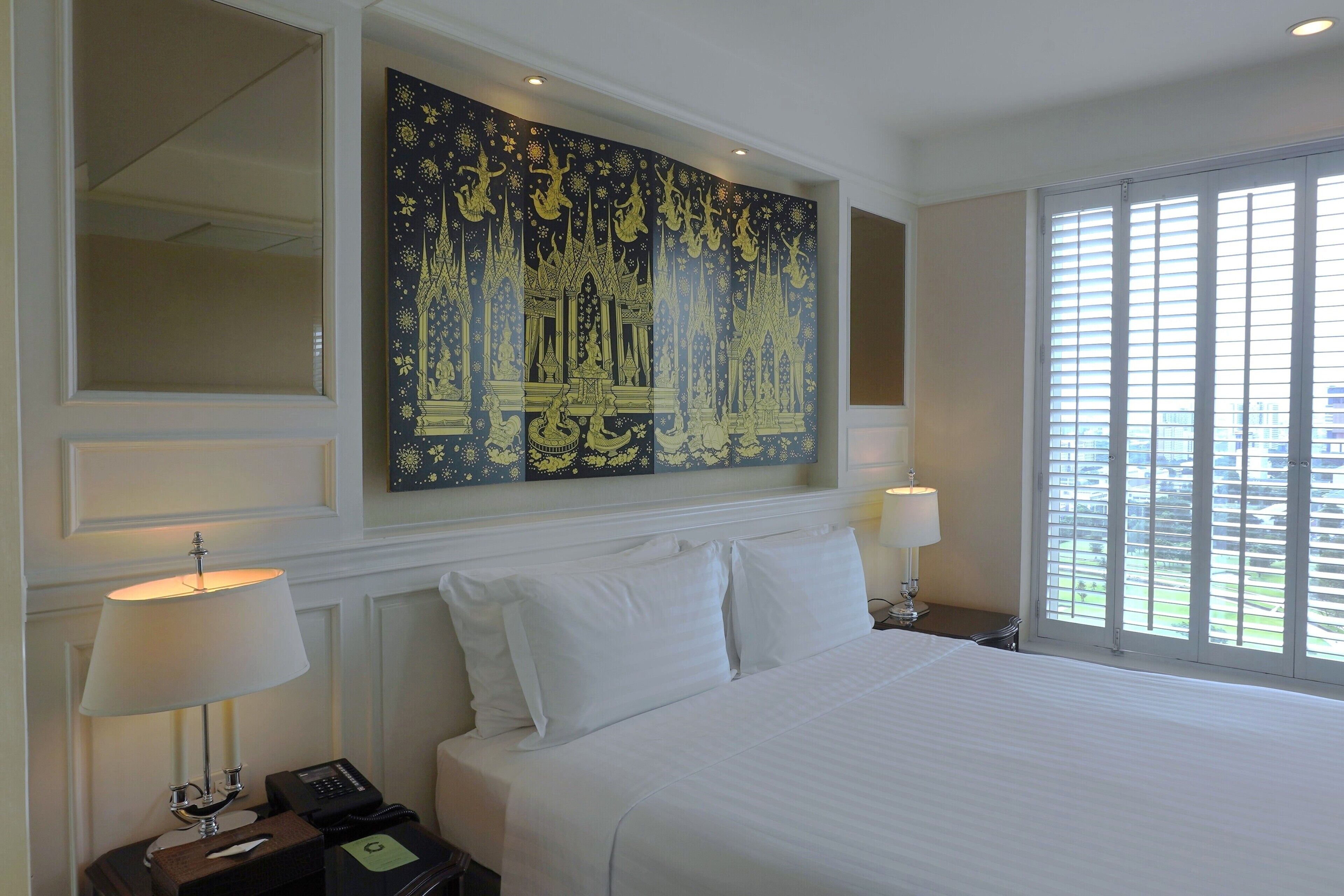 Habitación de hotel con una cama grande, dos lámparas de noche, un teléfono y una obra de arte en la pared que representa un edificio tradicional.