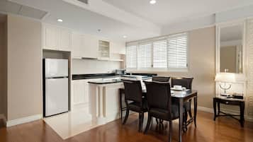 A modern kitchen with white cabinetry, a built-in refrigerator, a dining area with two chairs, and a small table with a lamp.