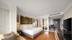A hotel room with a large bed, a sofa, a TV, and a dining area.
