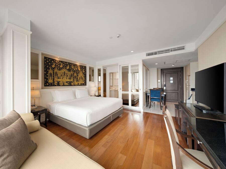 A hotel room with a large bed, a sofa, a TV, and a dining area.