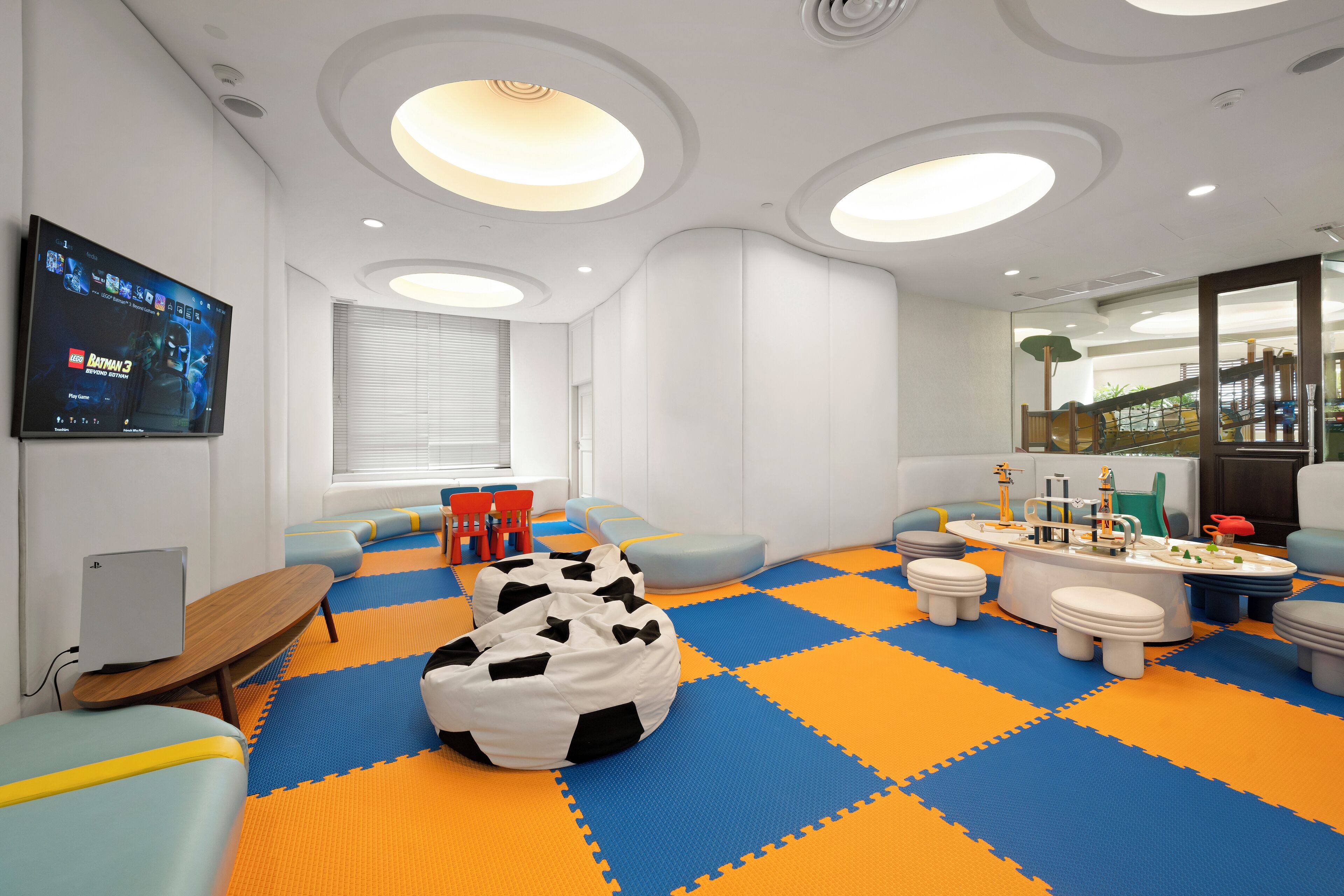 A modern children's playroom with a blue and orange foam floor, a large bean bag, and a play table.