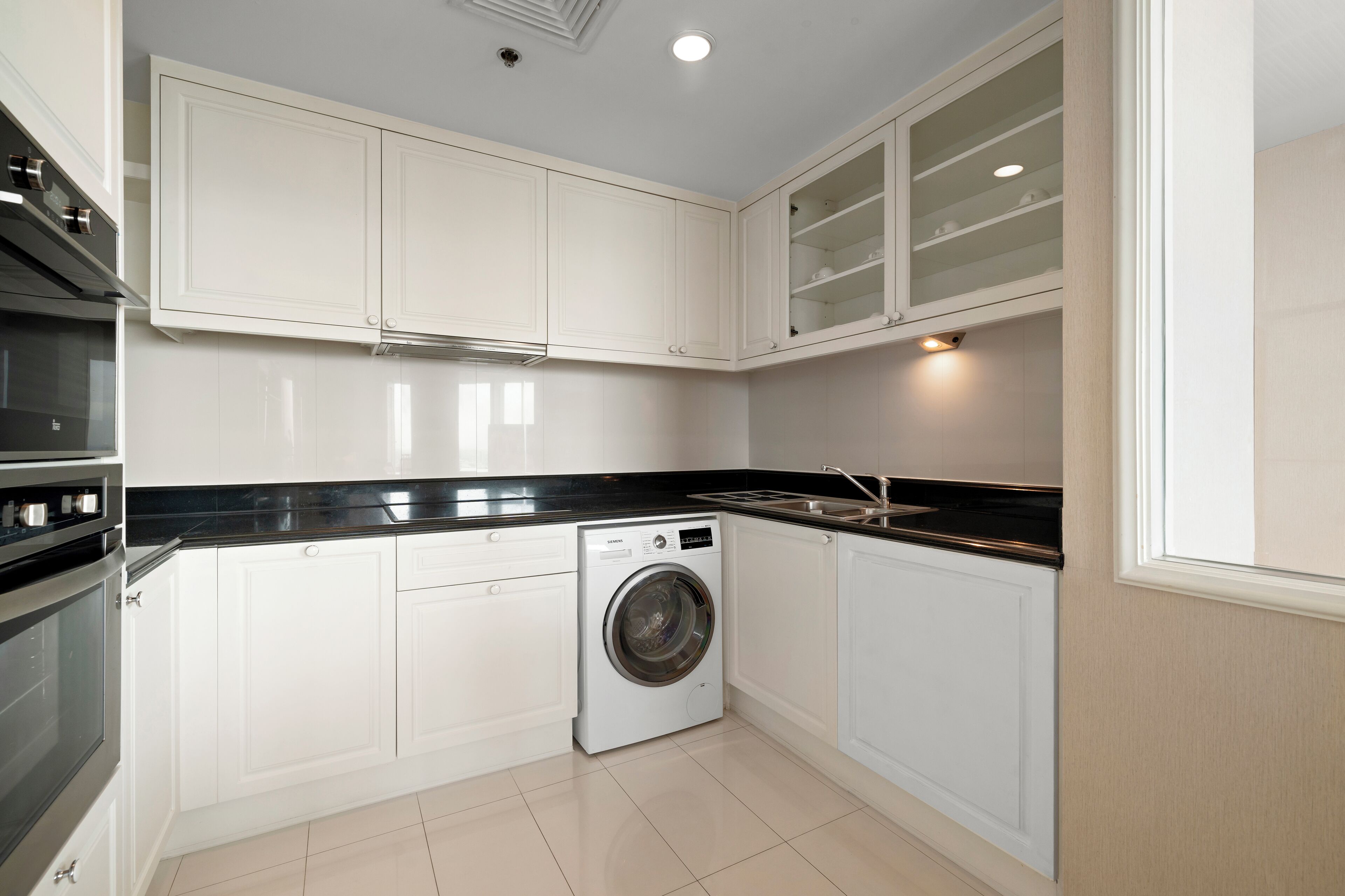 Une cuisine compacte avec des meubles blancs, un lave-linge encastré et un plan de travail noir.