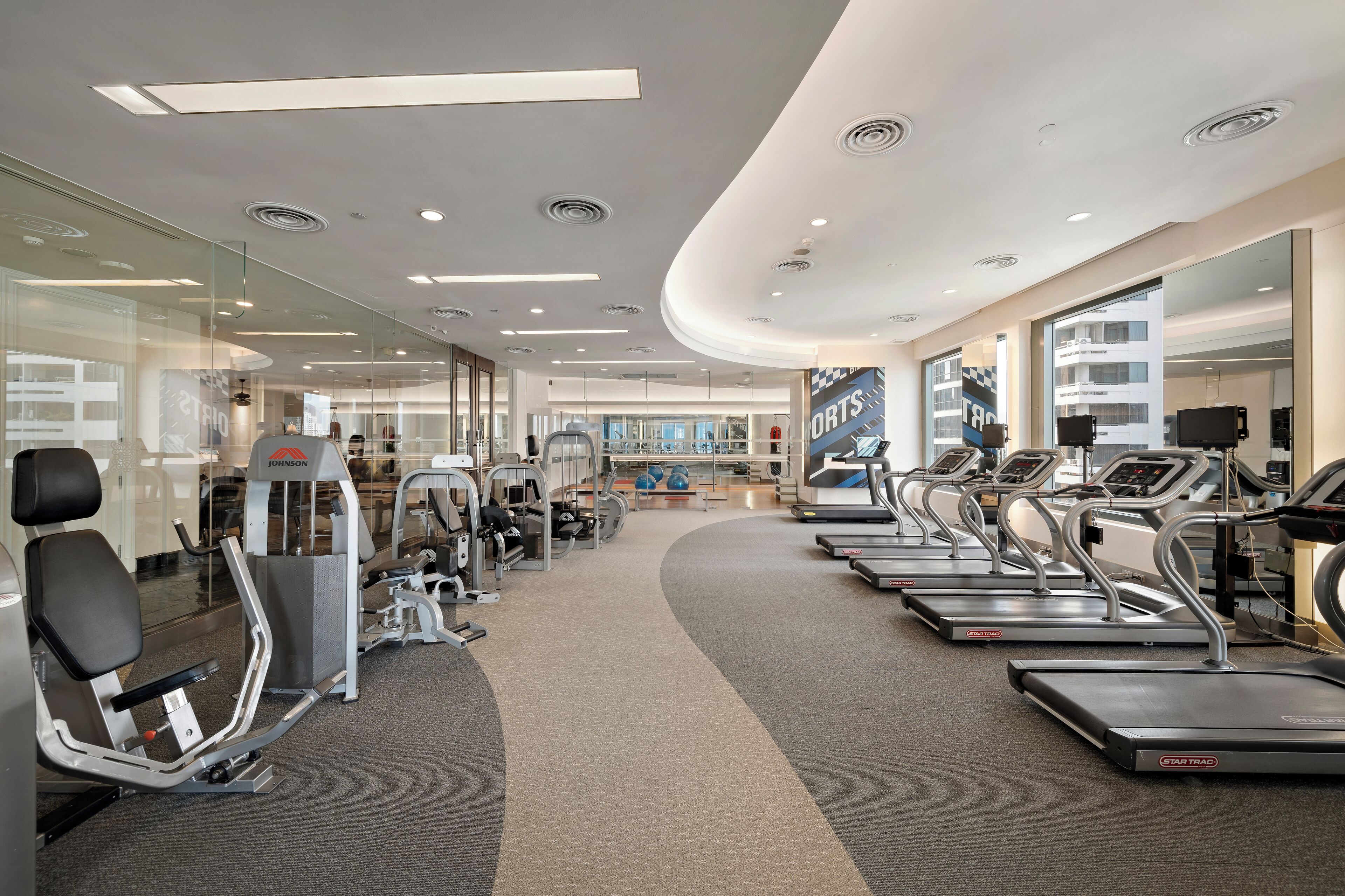 A modern gym with treadmills, weight machines, and a mirrored wall.