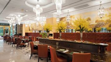 A spacious restaurant with high ceilings, ornate chandeliers, and a long counter with red upholstered seating.