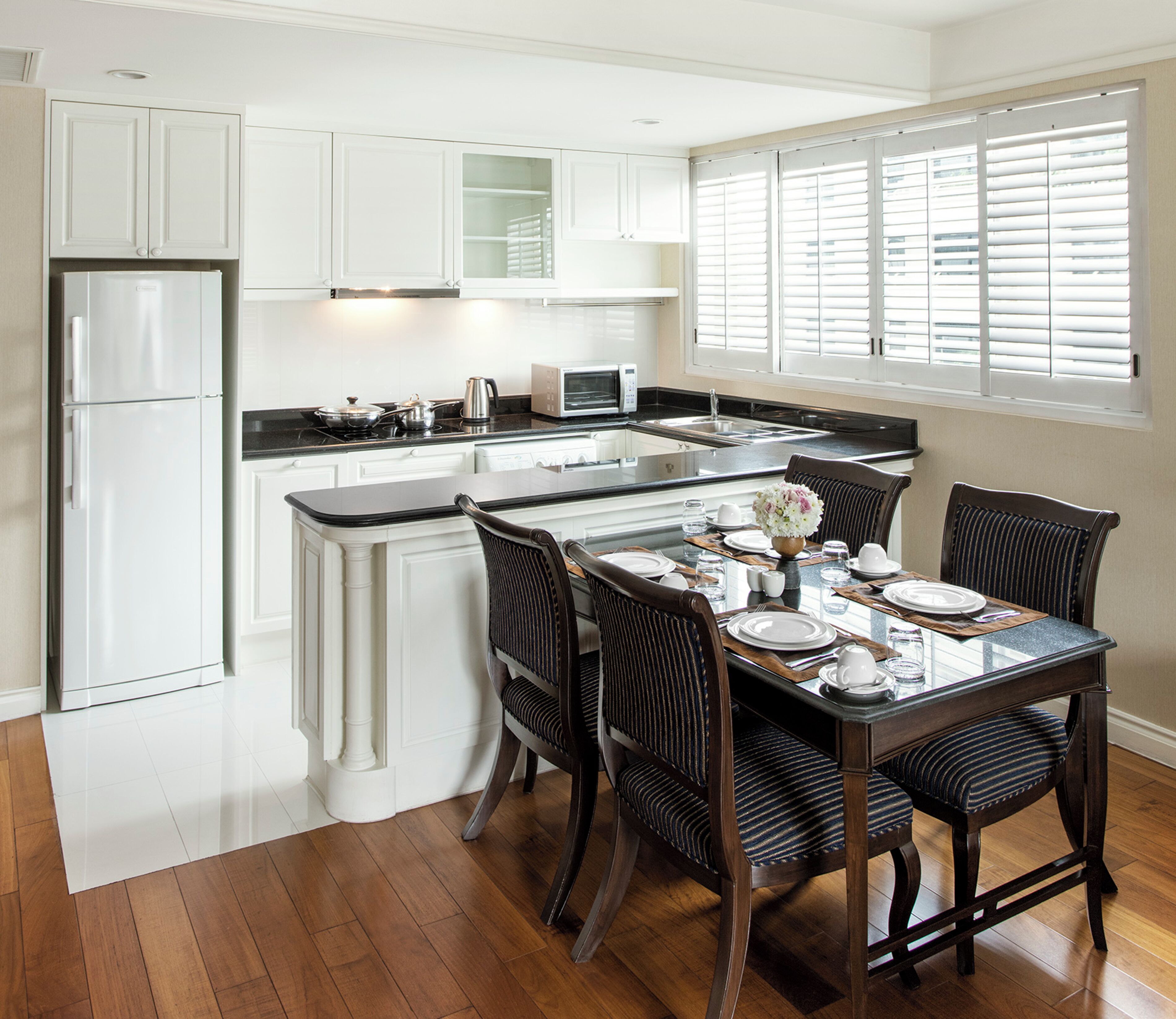 A modern kitchen with white cabinetry, a central island, and a dining area with a glass table and striped chairs.