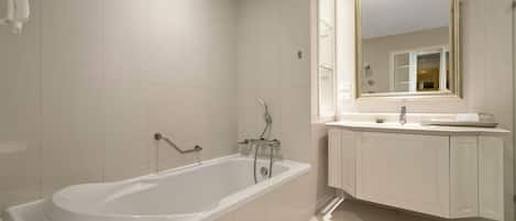 A modern bathroom with a large bathtub, a vanity with a mirror, and white tiled walls.
