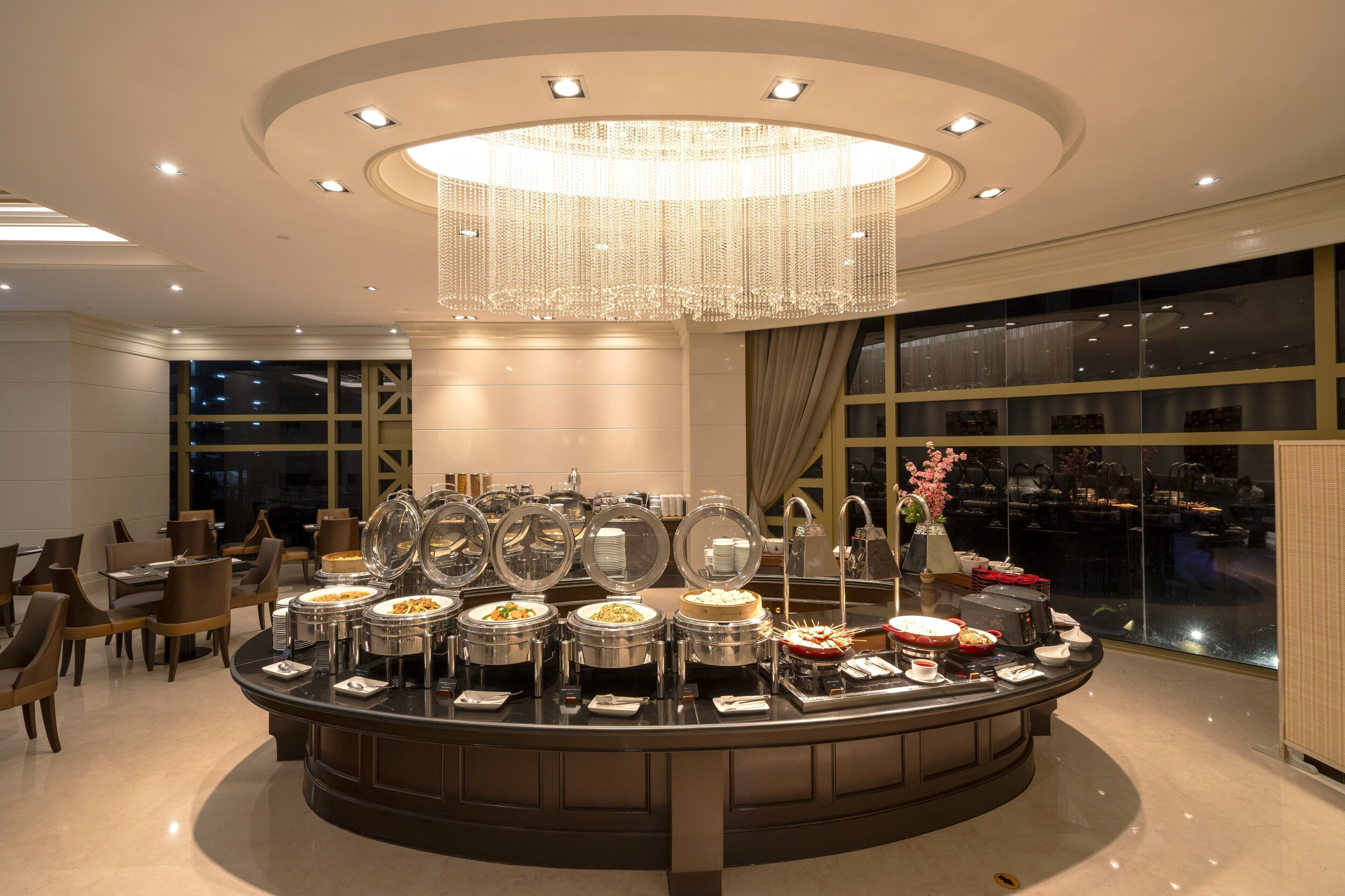 Un buffet disposé avec plusieurs points de service, un grand lustre et une vue sur le paysage urbain grâce à de grandes fenêtres.