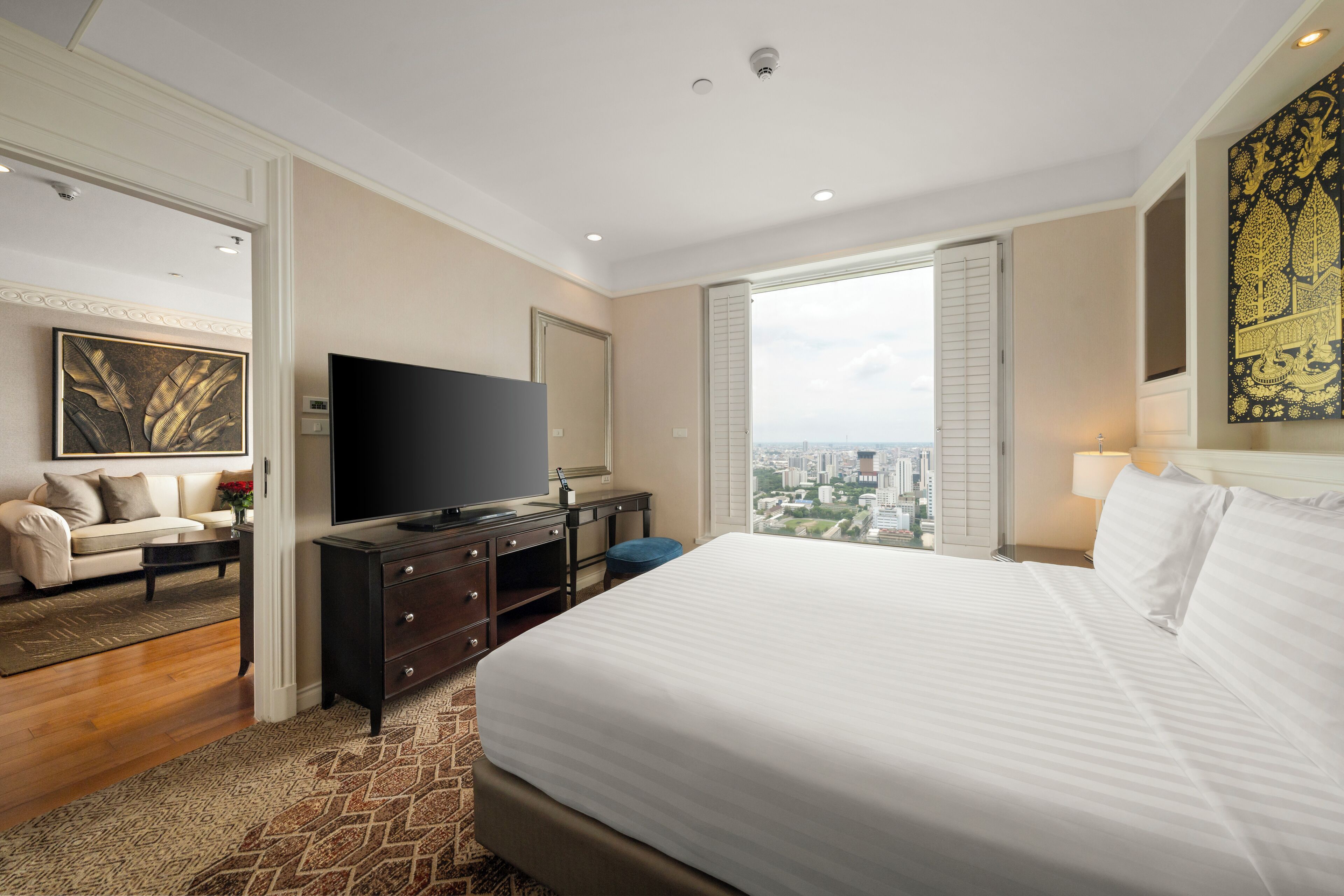 A hotel room with a large bed, a flat-screen TV, a dresser, a sofa, and a city view.