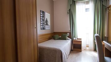 A hotel room with a bed, a desk, a chair, and a window with curtains.