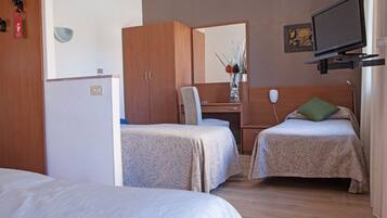 Una habitación de hotel con dos camas individuales, un escritorio con silla, un televisor montado en la pared y un armario.