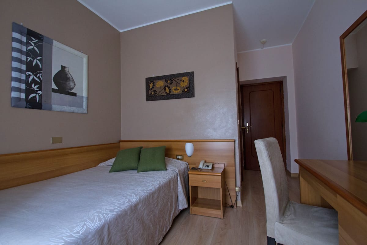 Habitación de hotel con cama, mesita de noche, silla y cuadros en las paredes.