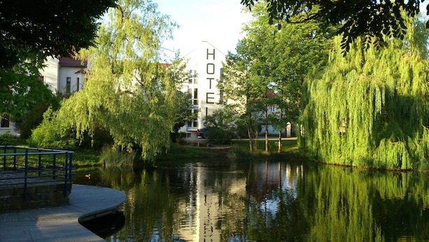 Een rustig uitzicht op de rivier met een hotelschilt, weelderige begroeiing en een kalm wateroppervlak dat de omgeving weerspiegelt.