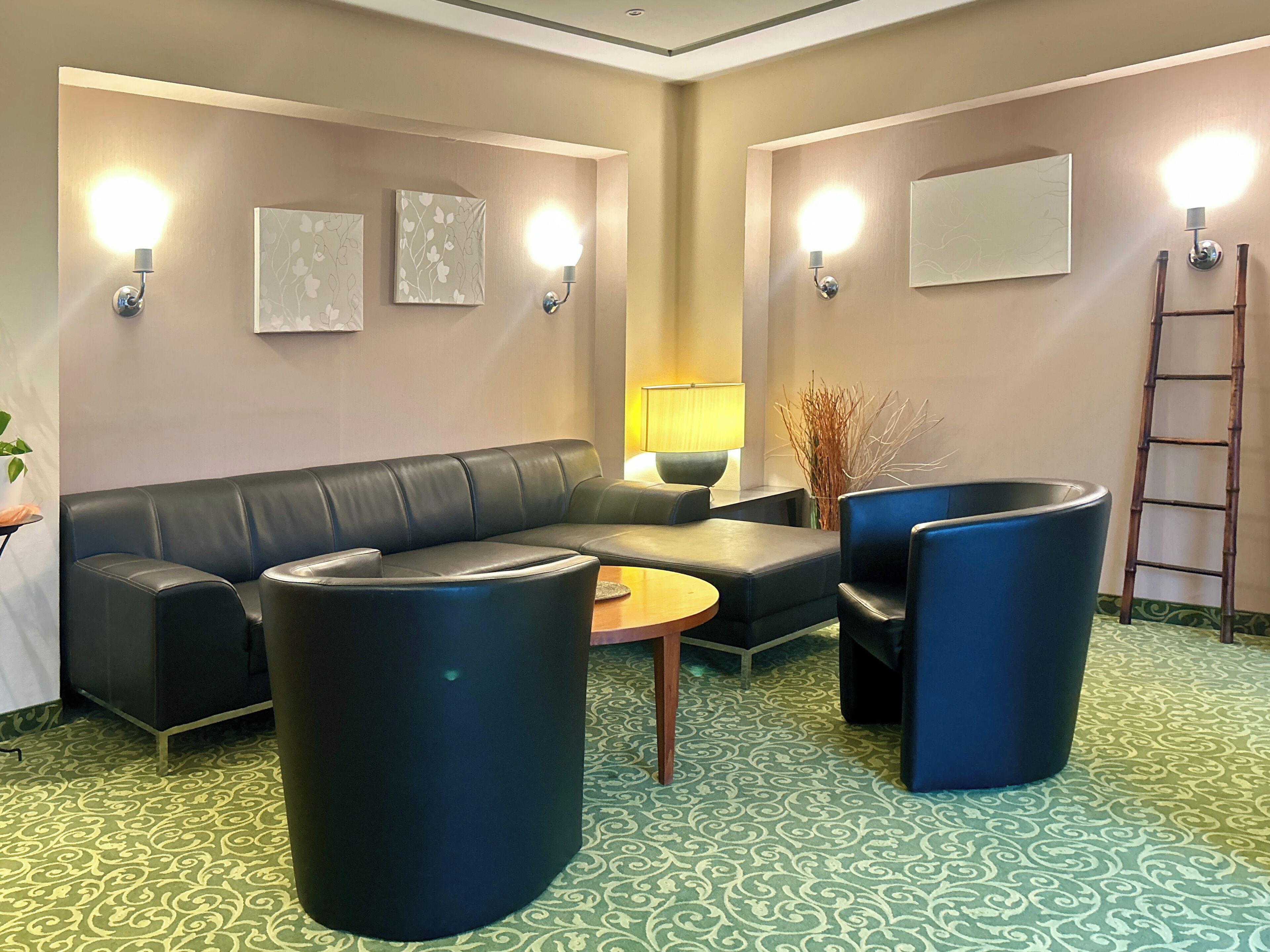 Un espacio lounge moderno con un sofá de cuero negro, dos sillones azules, una mesa de centro de madera y una alfombra estampada.