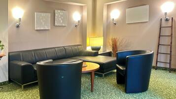 Un espacio lounge moderno con un sofá de cuero negro, dos sillones azules, una mesa de centro de madera y una alfombra estampada.