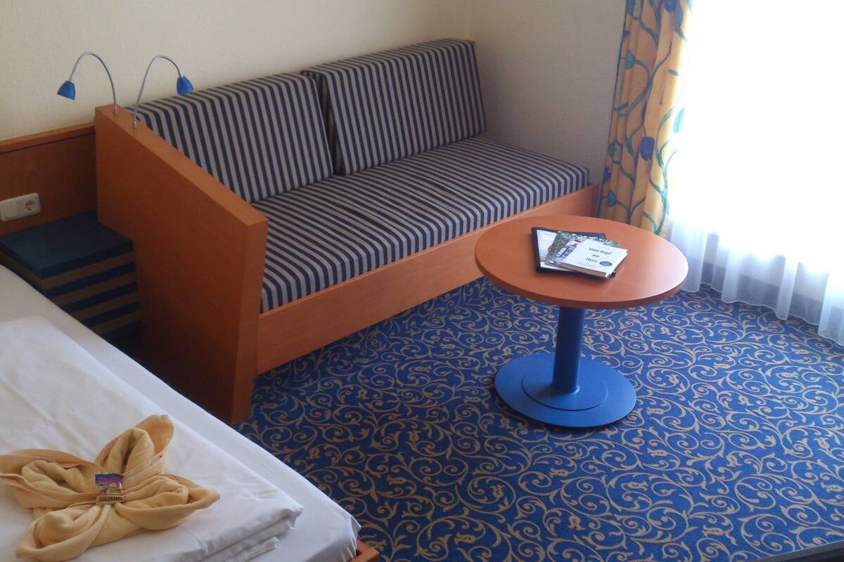 A hotel room with a bed, a sofa, a small table, and a patterned carpet.