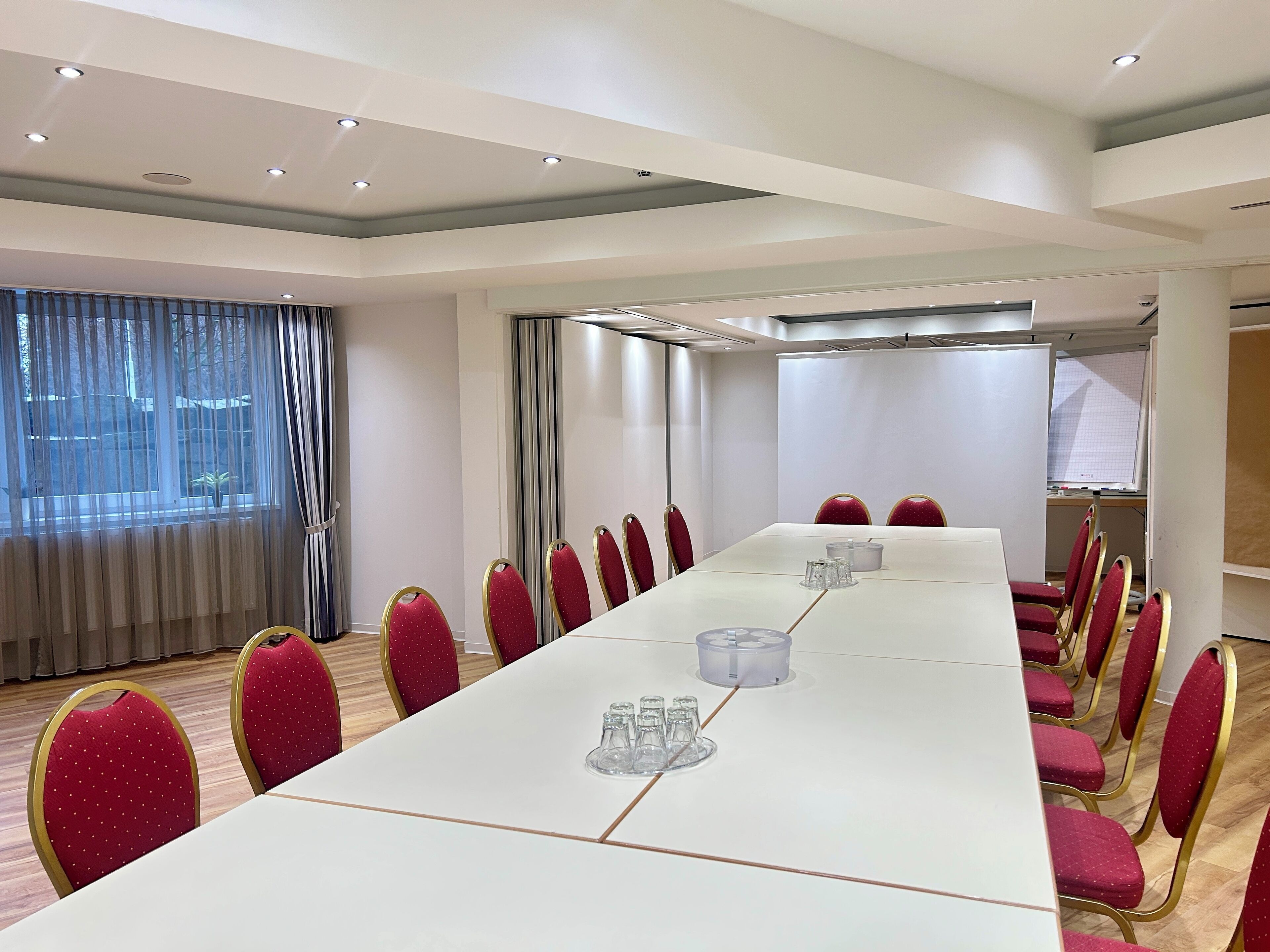 Un salón de conferencias con una mesa larga, sillas rojas y una pizarra.