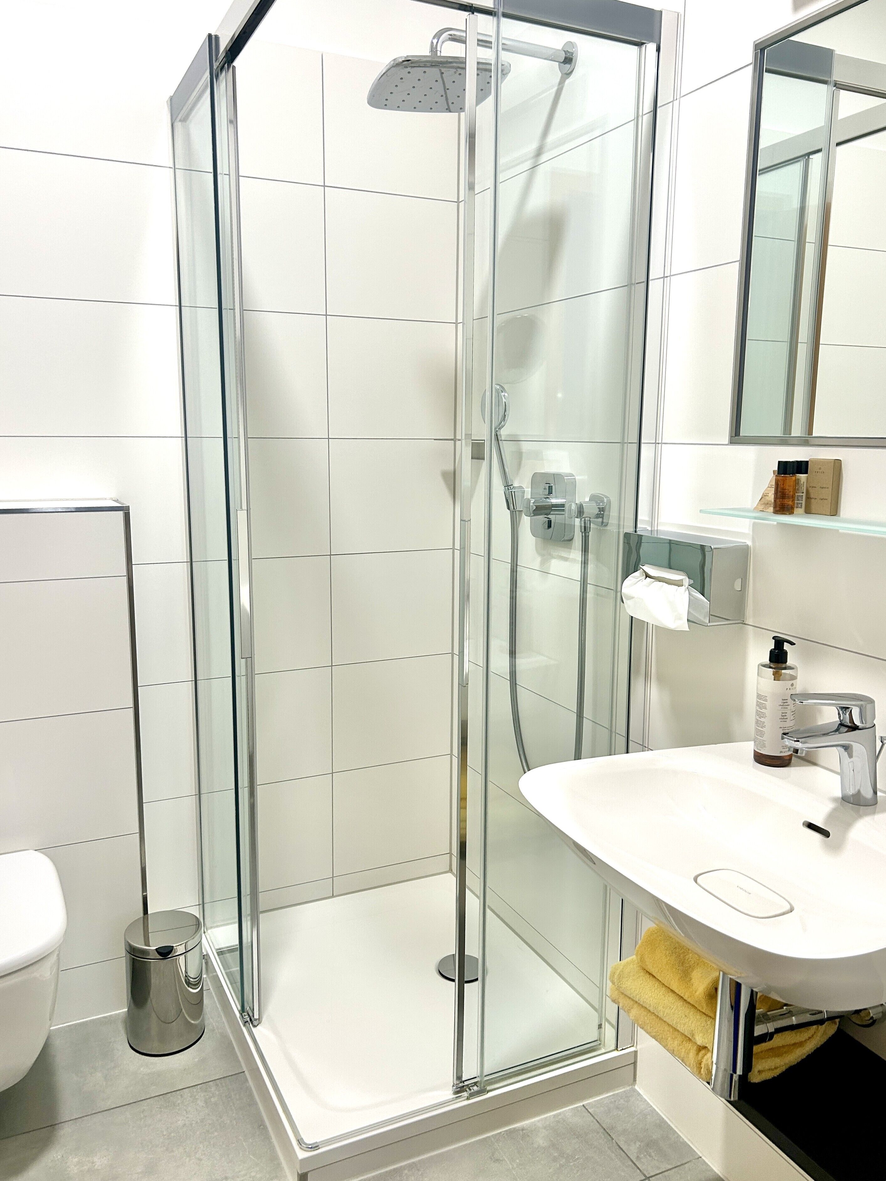 Un baño moderno con ducha de vidrio, lavamanos blanco y retrete.