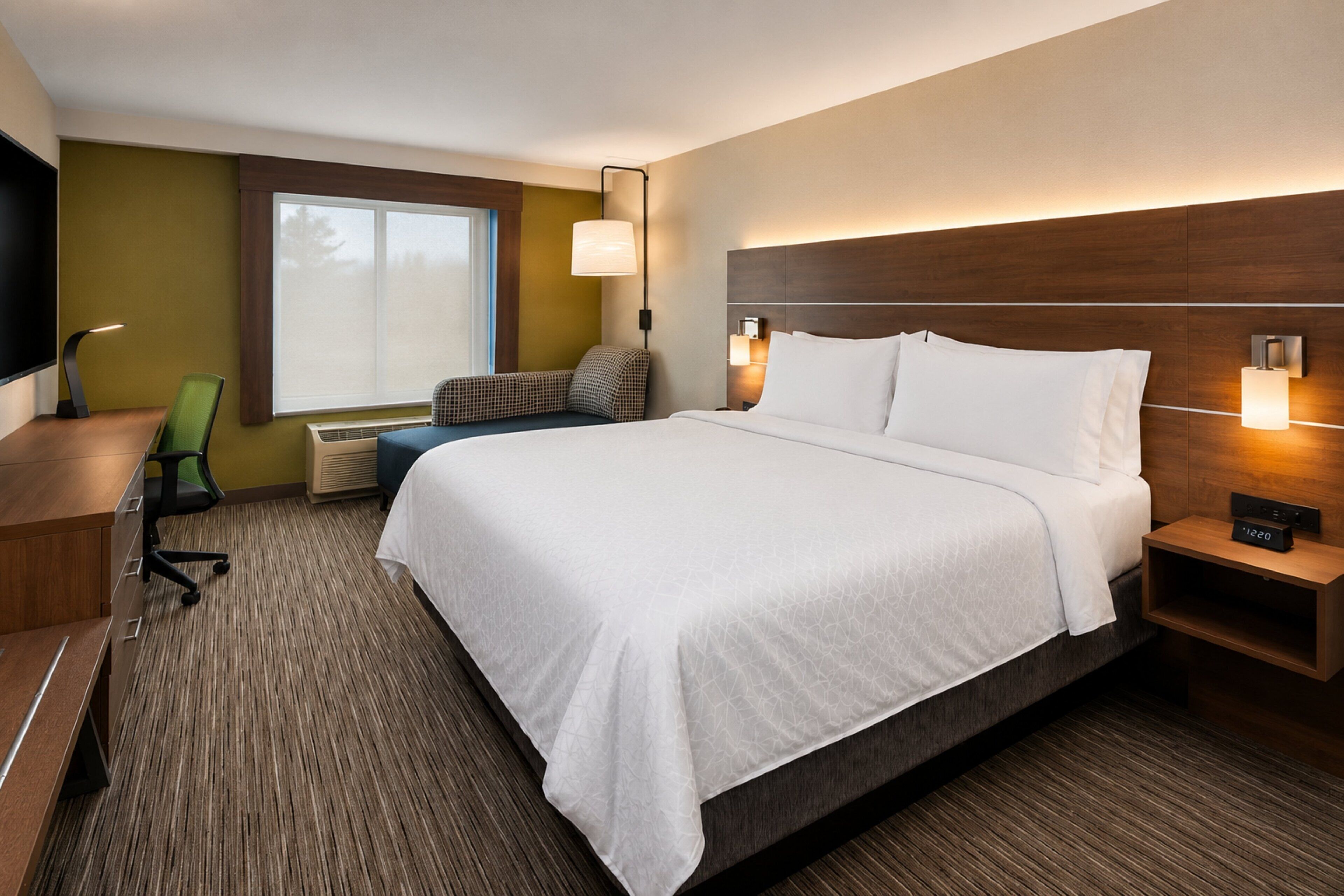 A hotel room with a large bed, a desk, a chair, a TV, and a window with blinds.