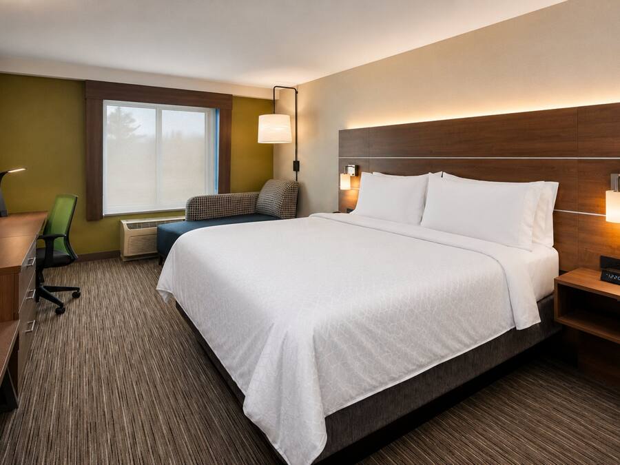 A hotel room with a large bed, a desk, a chair, a TV, and a window with blinds.