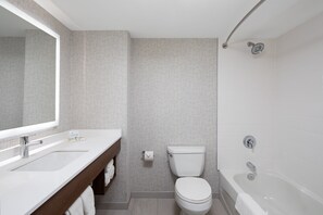 A modern bathroom with a white sink, toilet, and bathtub, featuring a large mirror and a towel rack.