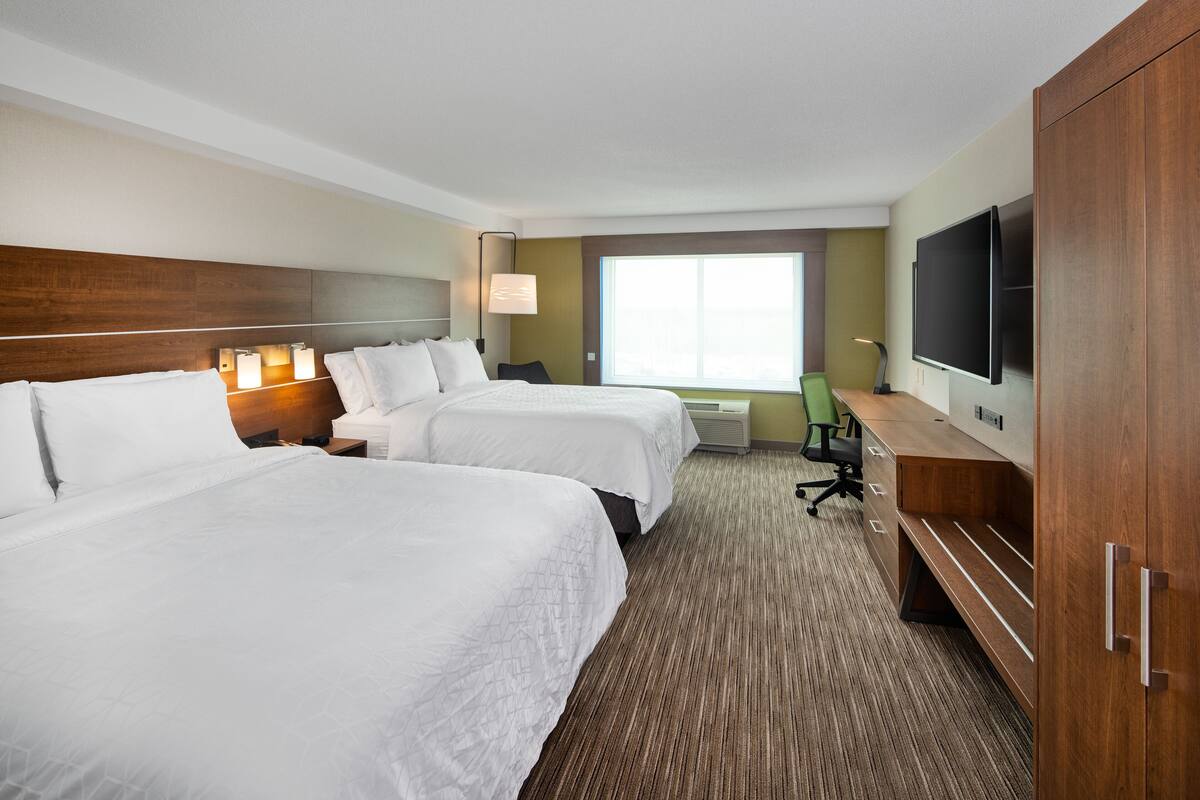 A hotel room with two beds, a desk, a TV, and a large window.