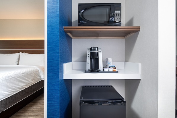 A hotel room with a bed, a microwave, a coffee maker, and a small storage bin.