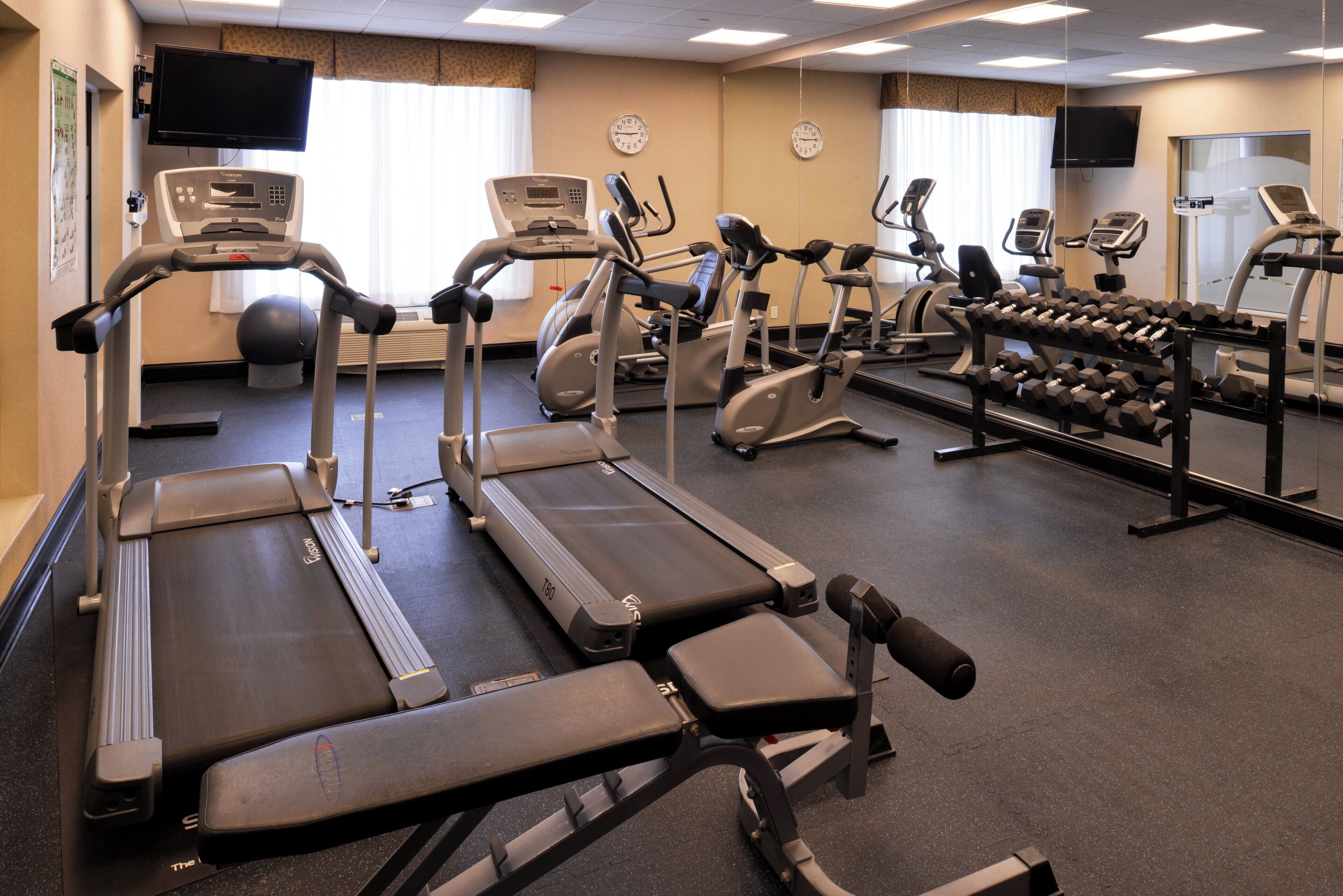 Un gimnasio con cintas de correr, elípticas y una banca para pesas.