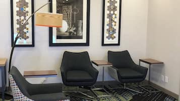 A hotel room with two armchairs, a small table, a floor lamp, and three framed artworks on the wall.