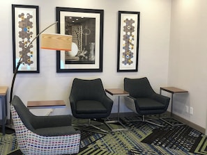 A hotel room with two armchairs, a small table, a floor lamp, and three framed artworks on the wall.