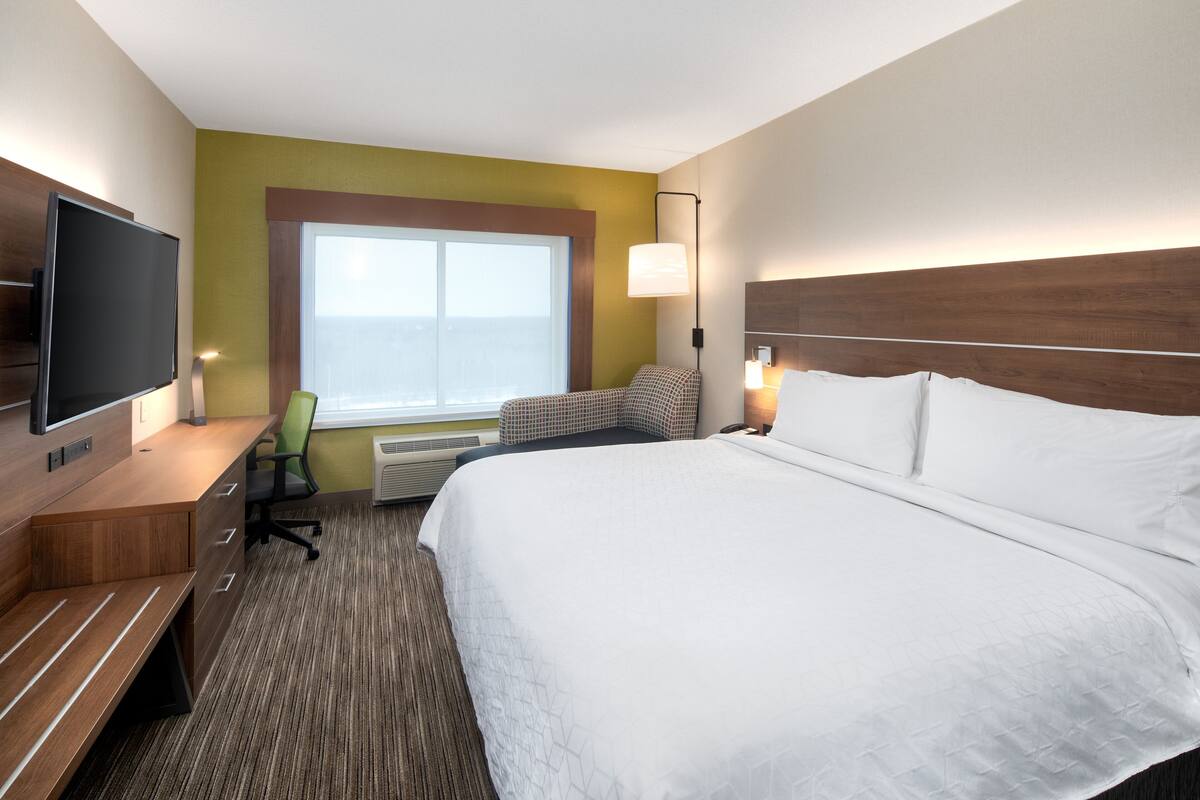A hotel room with a large bed, a desk, a chair, a flat-screen TV, and a window with a view.