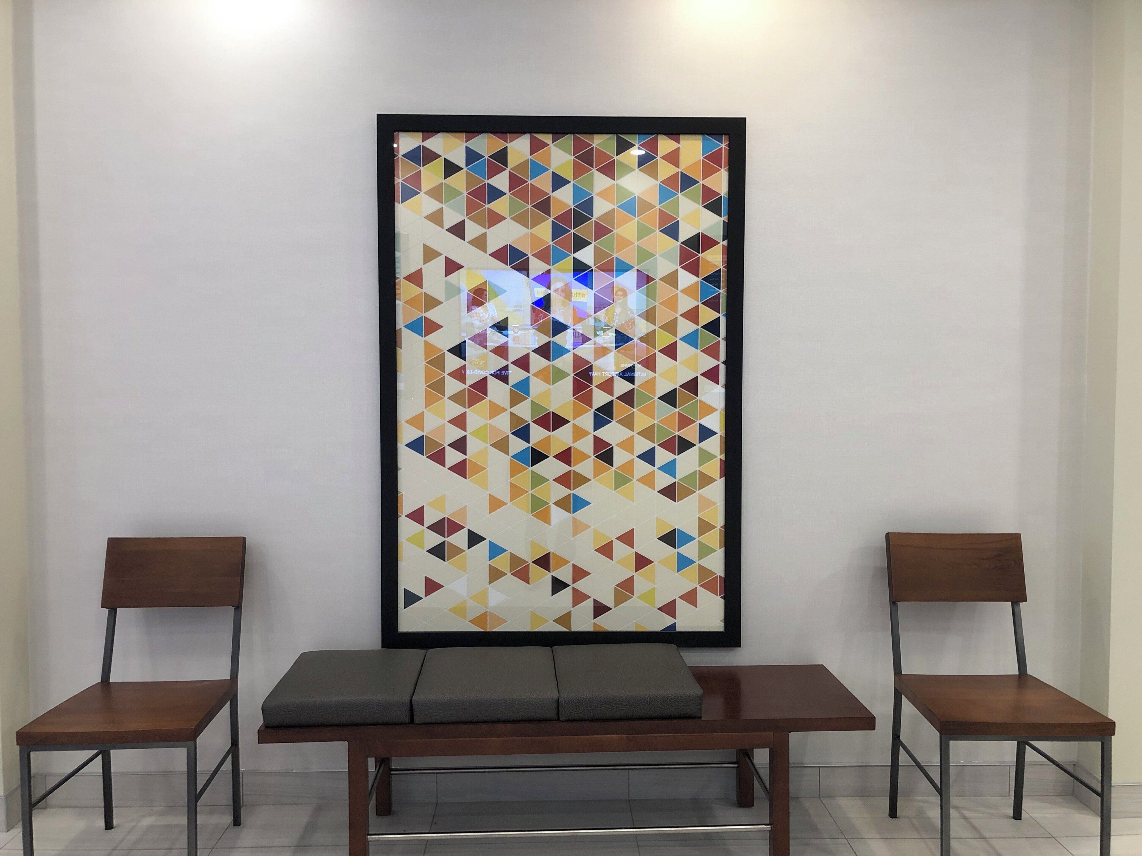 Una habitación con una obra de arte geométrica enmarcada en la pared, dos sillas de madera y un banco.