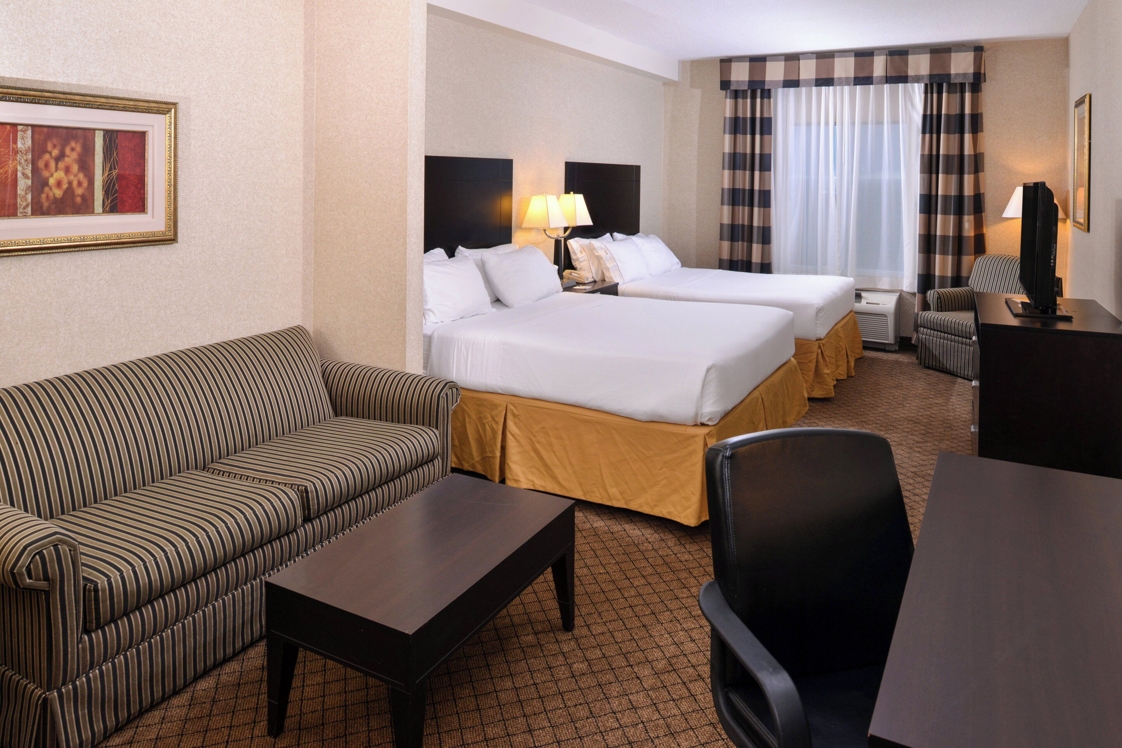 A hotel room with two beds, a sofa, a desk, a chair, and a television.
