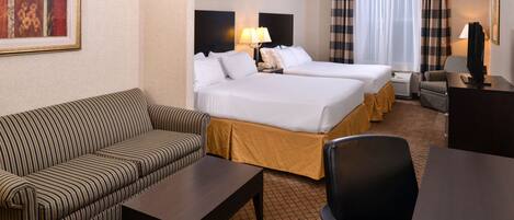 A hotel room with two beds, a sofa, a coffee table, a TV, and a desk.
