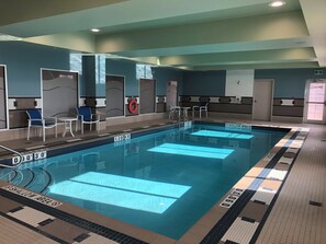 Une piscine intérieure avec des couloirs délimités, des chaises et un panneau indiquant la zone peu profonde.