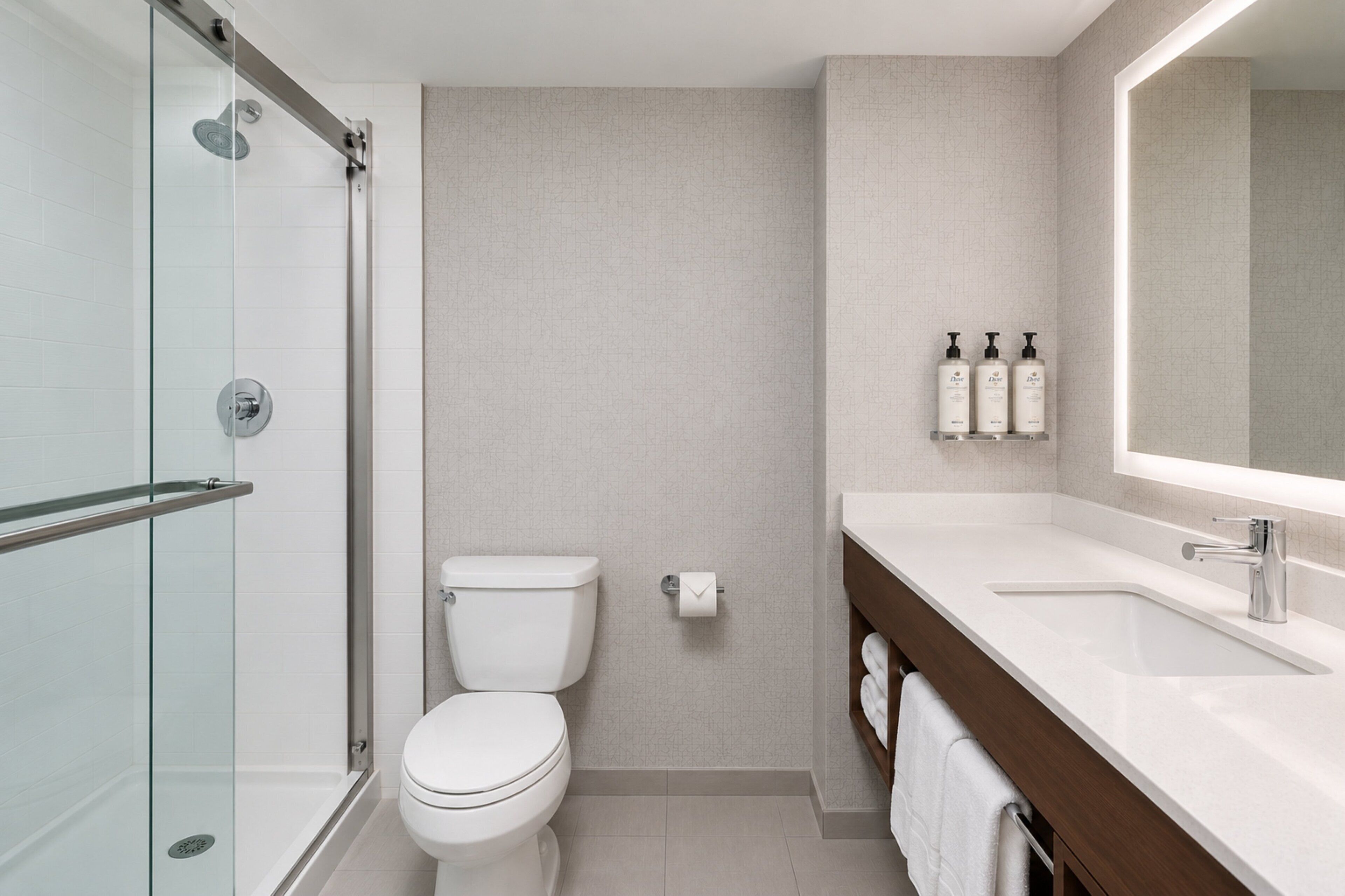 A modern bathroom with a glass shower enclosure, a white toilet, and a vanity with a large mirror and toiletries.