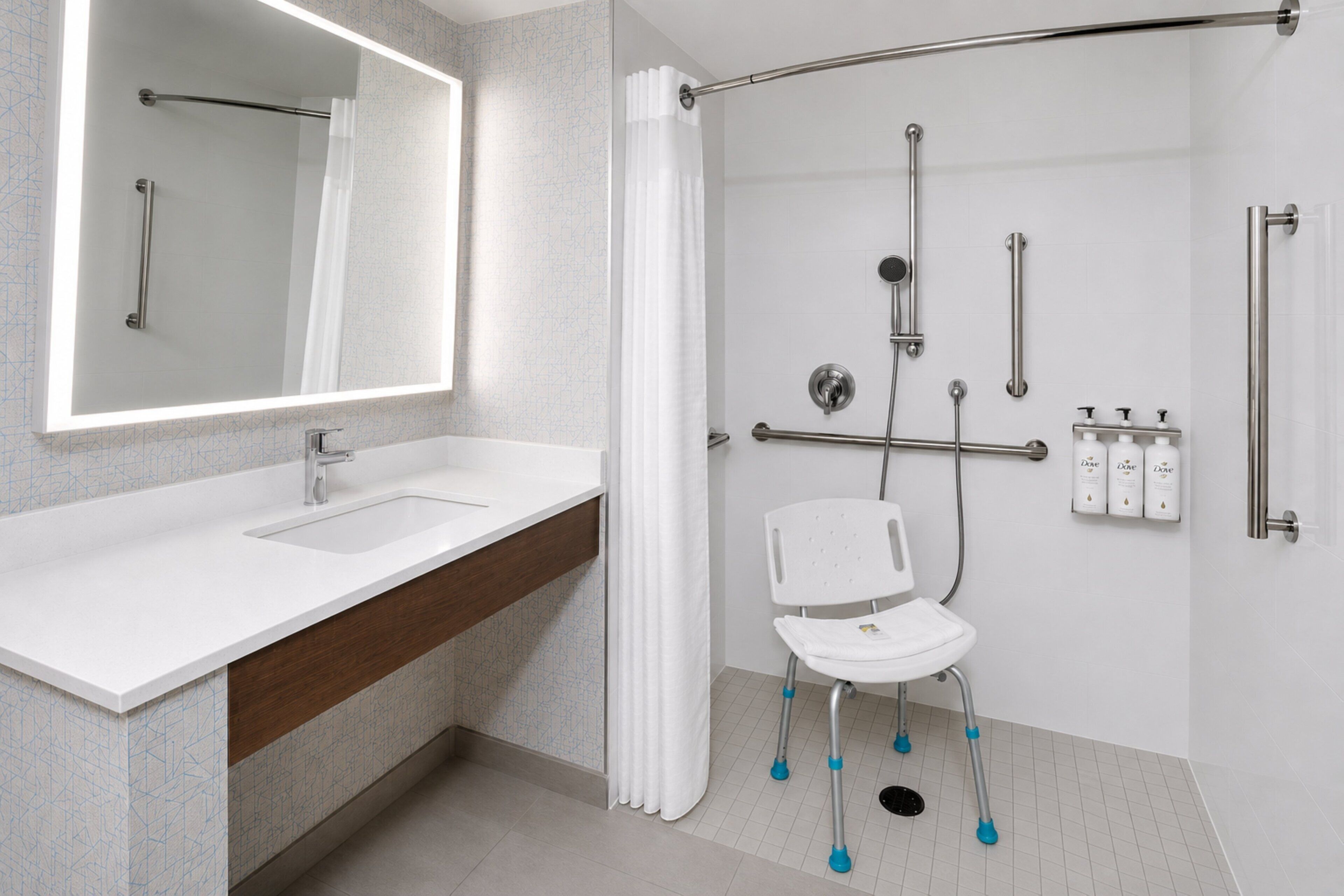 A modern bathroom with a large mirror, a sink, a shower with grab bars, and a white chair.