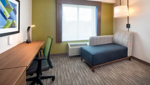 A hotel room with a desk, chair, sofa, window, lamp, and air conditioning unit. - Holiday Inn Express & Suites Halifax Airport by IHG (Goffs)