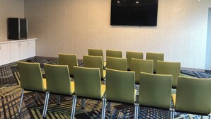 A conference room with a flat-screen TV mounted on the wall, a row of green chairs, and a patterned carpet. - Holiday Inn Express & Suites Halifax Airport by IHG (Goffs)