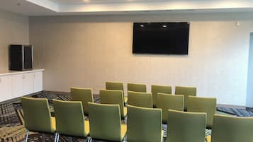 Une salle de conférence équipée d’un téléviseur à écran plat fixé au mur, d’une rangée de chaises vertes et d’une moquette à motifs.