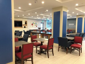A modern cafe with multiple tables and chairs, a flat-screen TV mounted on the wall, and a 'Good Morning' sign on the wall. - Holiday Inn Express & Suites Halifax Airport by IHG (Goffs)