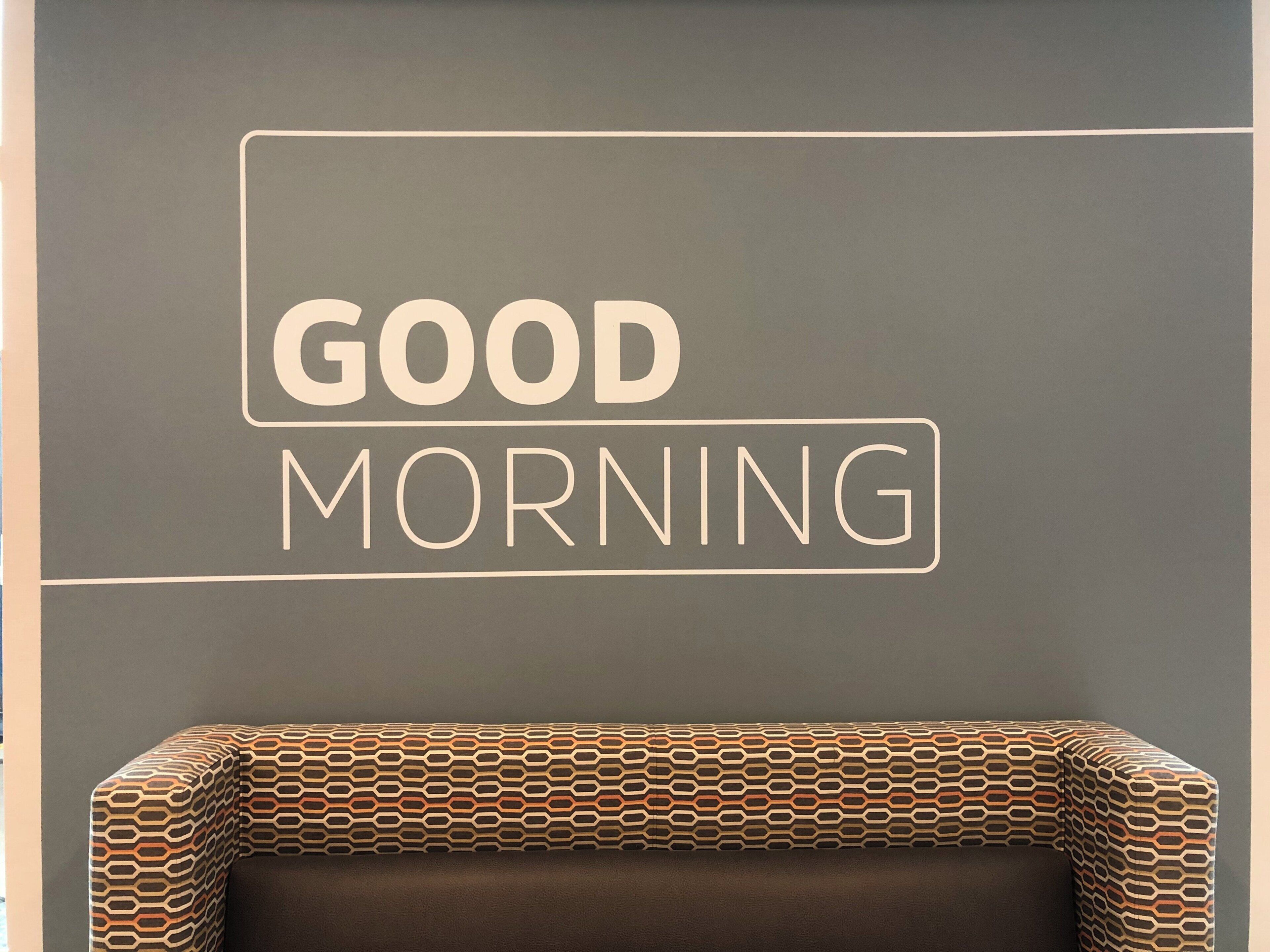 Eine Wand mit dem Schriftzug 'GOOD MORNING' und einem gemusterten Kissen.